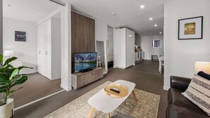 A modern living room with a TV, a coffee table, and a sofa. There is a kitchen area in the background.