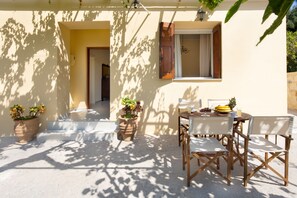 A patio with a table and chairs, potted plants, and a window with shutters.