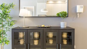 Una habitación moderna con un mueble oscuro, un espejo, una lámpara, una planta en maceta y un teléfono en la pared.