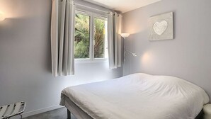A bedroom with a bed, a window with curtains, a bedside lamp, and a wall-mounted heart decoration. - Berlioz Garden - Jardin,Free Parking,AC,Wifi (Antibes)