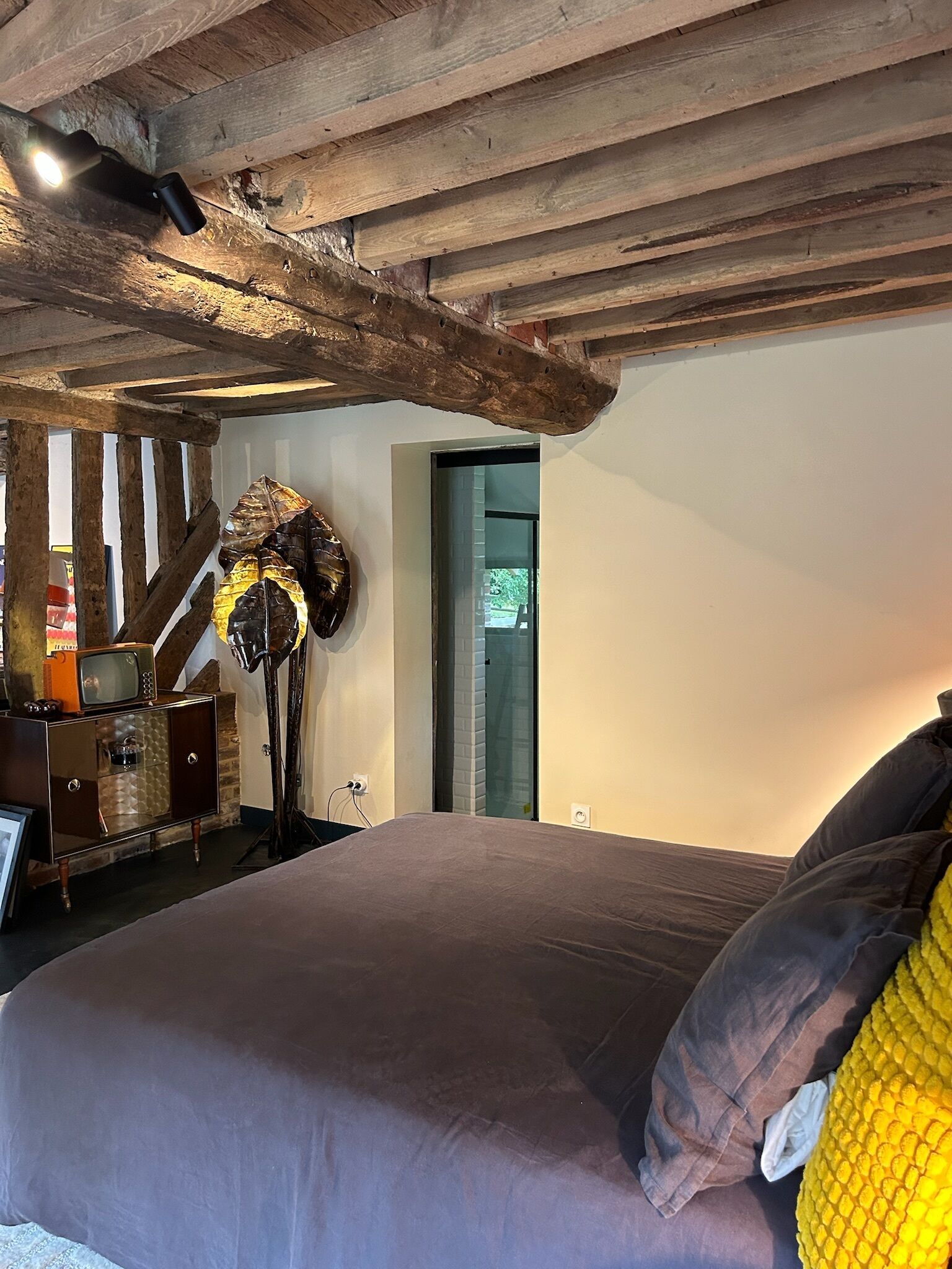 A bedroom with a wooden ceiling, a bed with a brown mattress and pillows, a vintage radio, and a mirror.