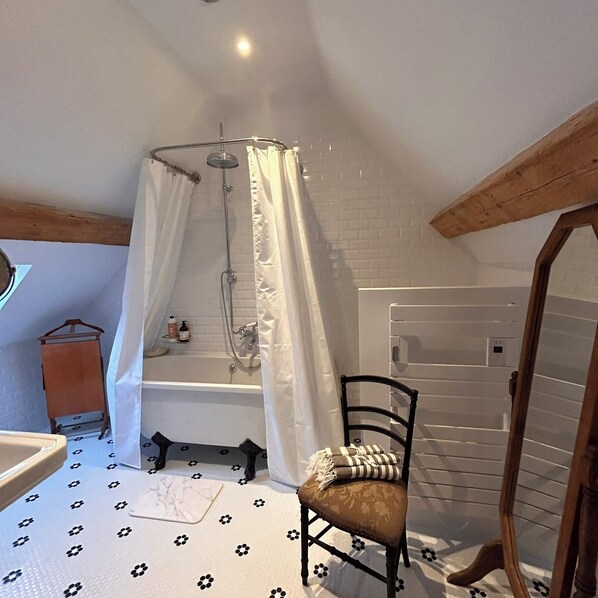 Un baño con bañera, ducha, una silla y estructura de vigas de madera.