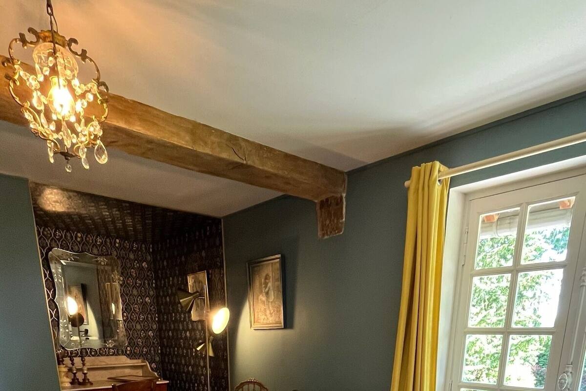 A bedroom with a large bed, a desk with a chair, a radiator, and a window with curtains.