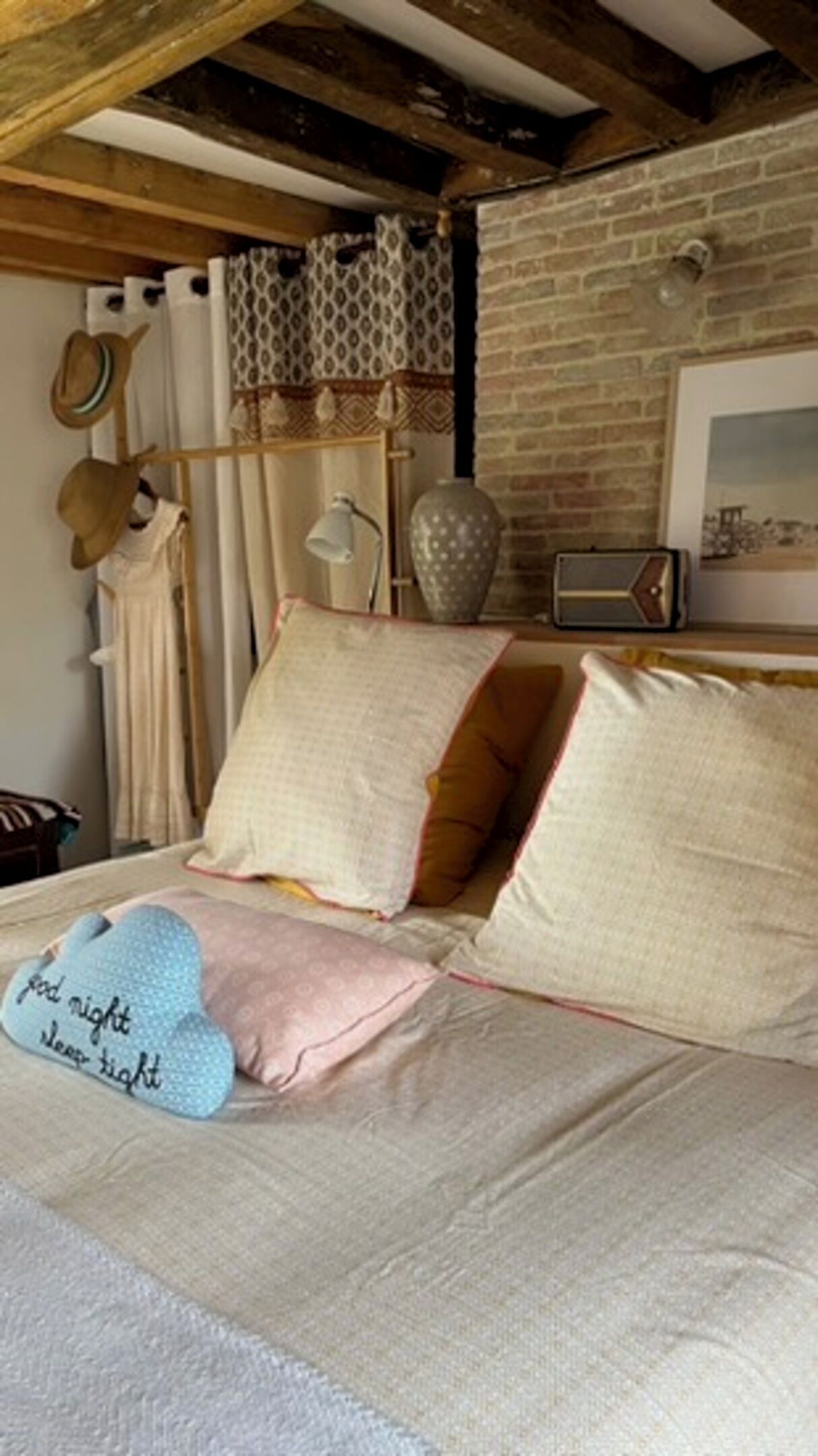 A cozy bedroom with a bed, pillows, a hat rack, and a lamp.