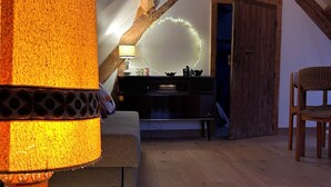 A cozy attic room with exposed wooden beams, a round mirror with LED lights, a sofa, a chair, and a decorative lamp. - Domaine de Blanvatel (Saint-Pierre-en-Auge)