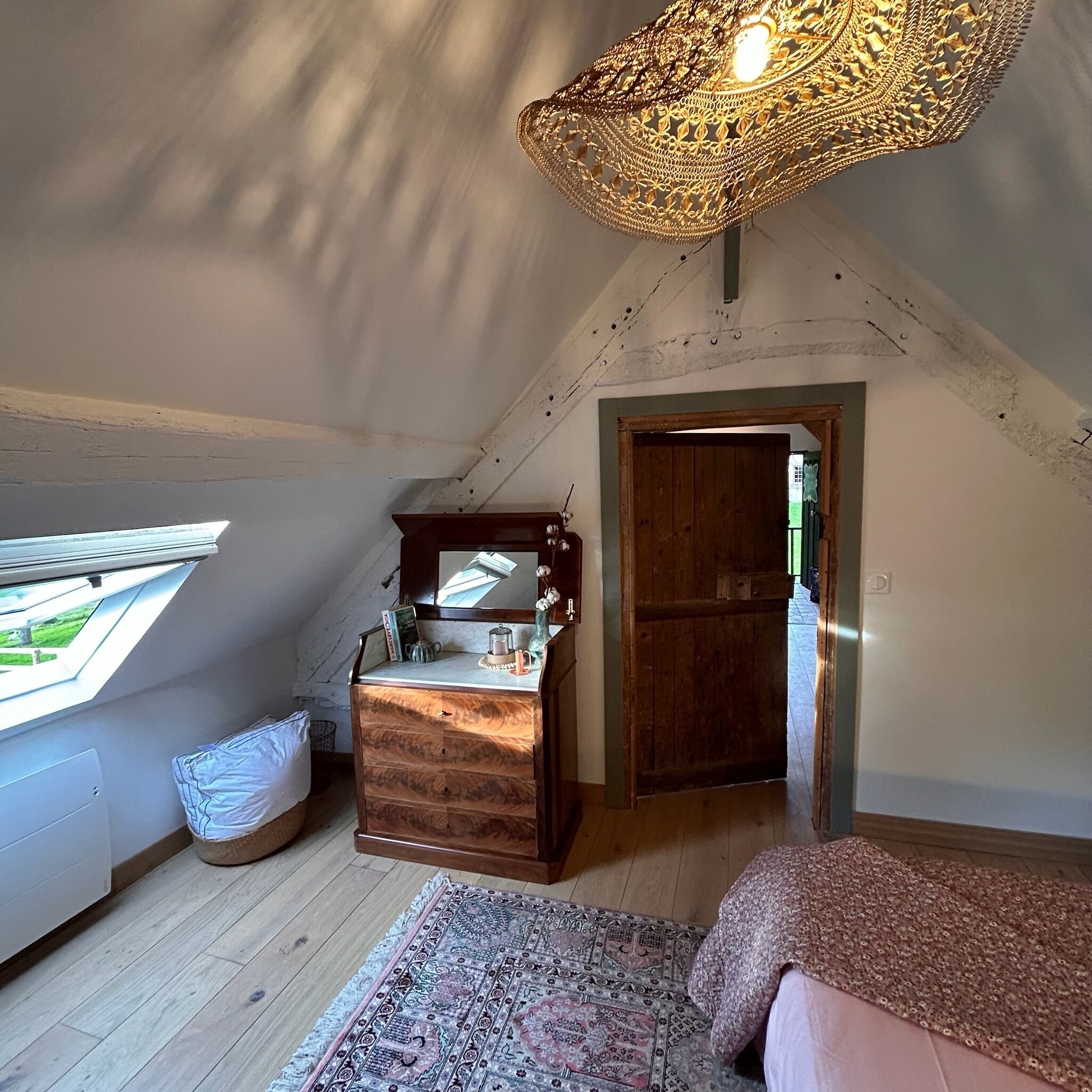 Ein gemütliches Schlafzimmer im Dachgeschoss mit einem Holzkasten, einem großen Fenster, einer Pendelleuchte und einem gemusterten Teppich.