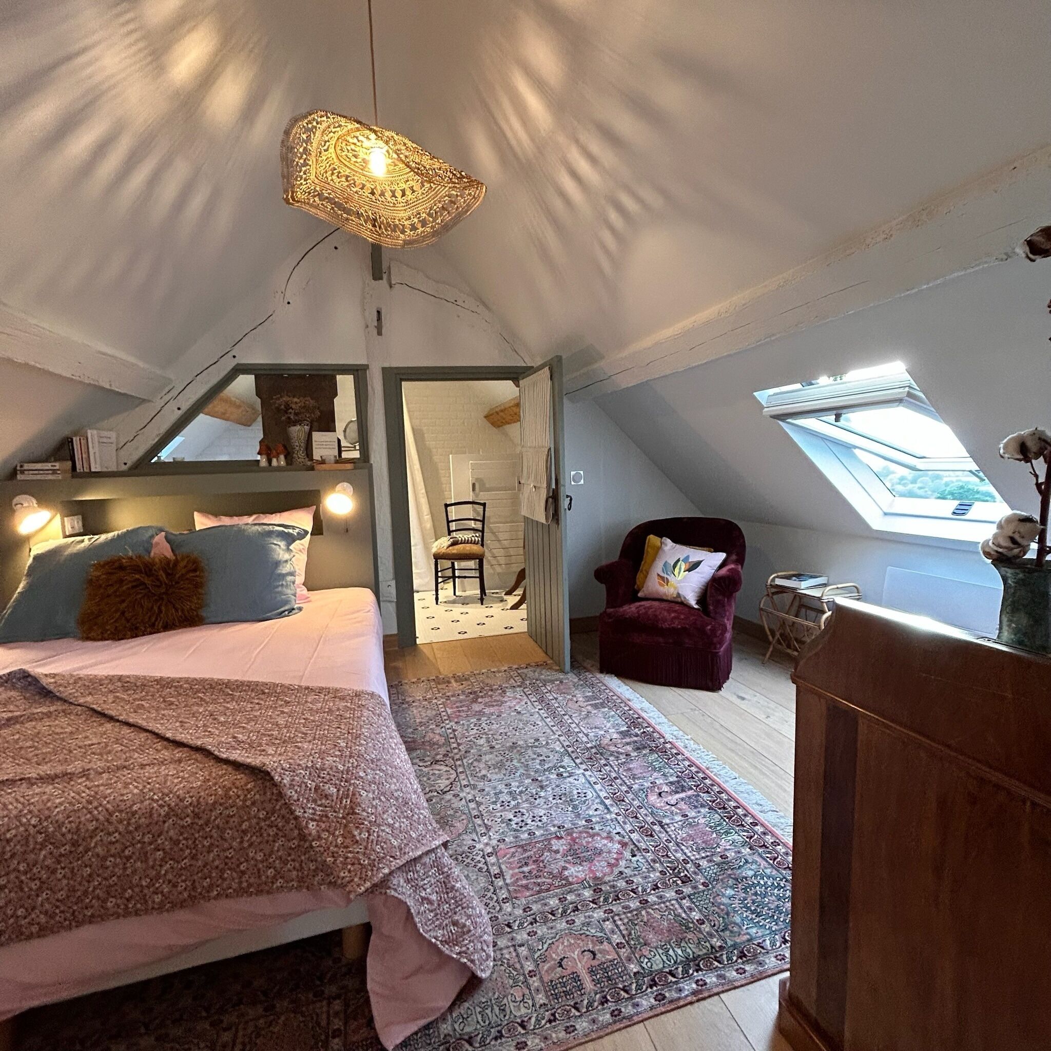 A cozy attic bedroom with a bed, a chair, and a skylight.