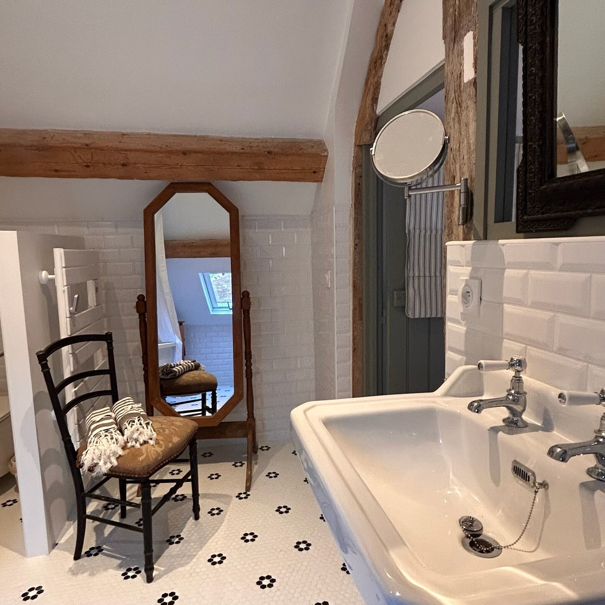 Un baño con lavabo blanco, vigas de madera, un espejo y una silla con cojín estampado.