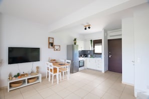 A modern kitchen with white cabinets, a built-in oven, and a refrigerator. There is a dining table with chairs and a flat-screen TV mounted on the wall. - Calas Sani Villas (Sane)
