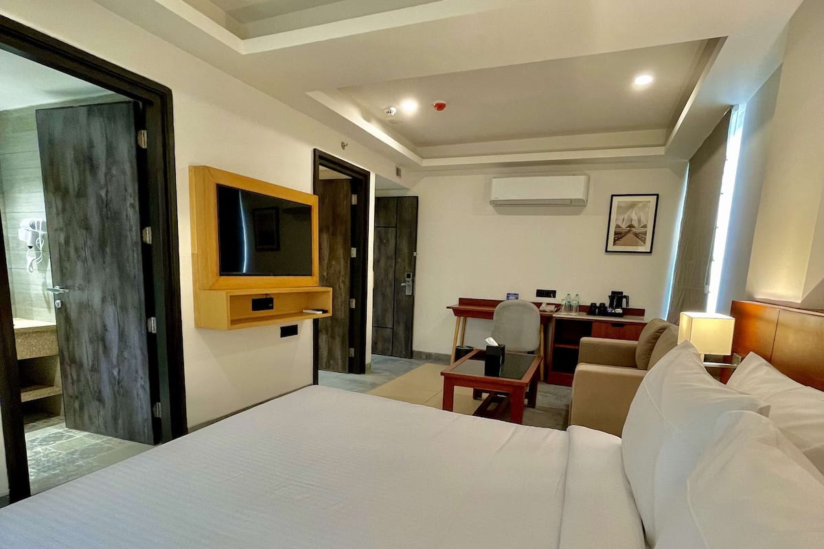 A hotel room with a large bed, a TV mounted on the wall, a desk with a chair, and a small table.