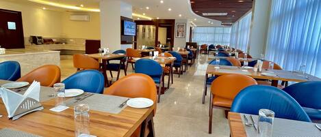 A modern dining area with wooden tables and blue chairs, featuring a curved ceiling and large windows.