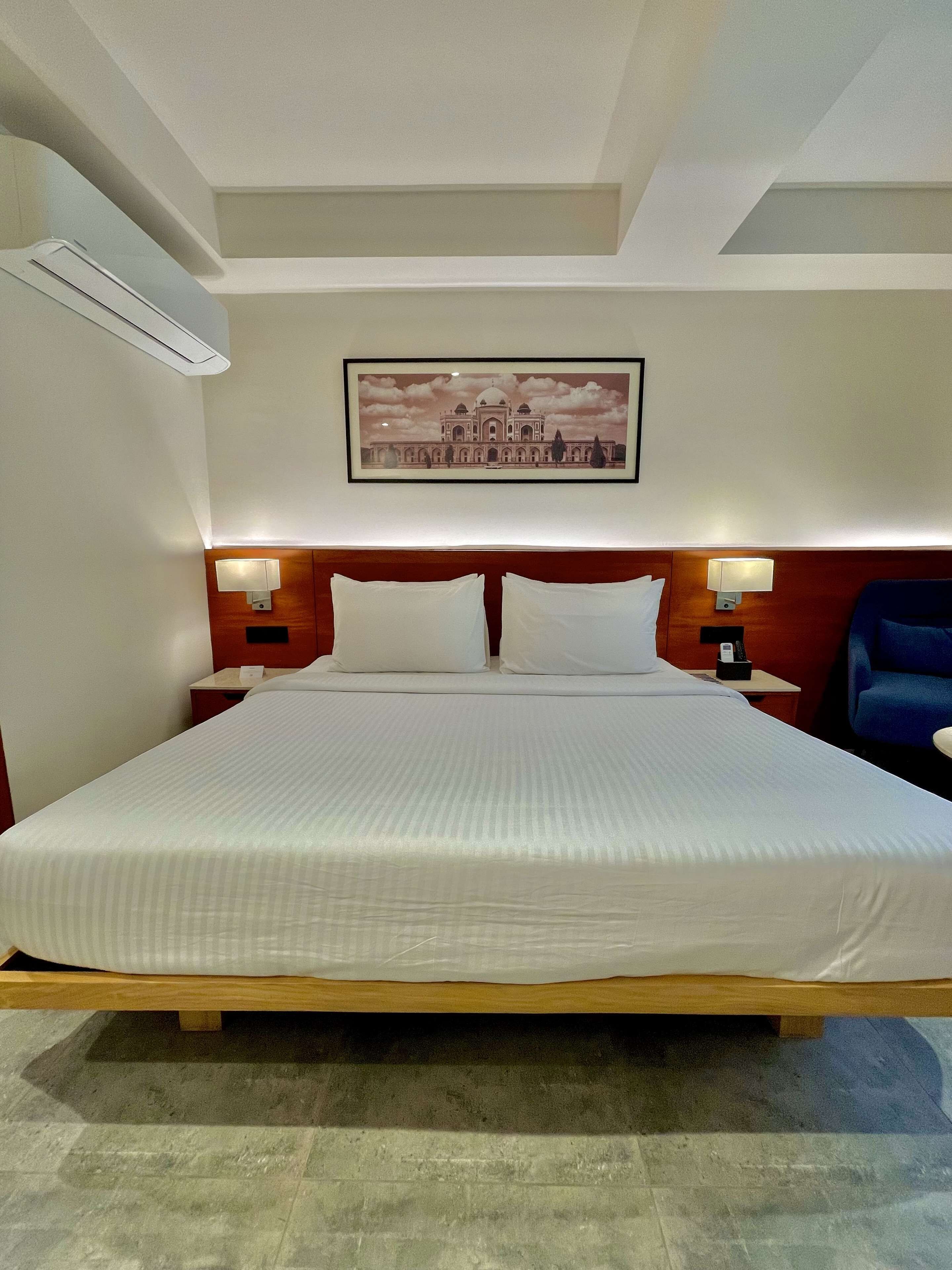 A hotel room with a large bed, two bedside tables with lamps, a framed picture on the wall, and a blue chair.