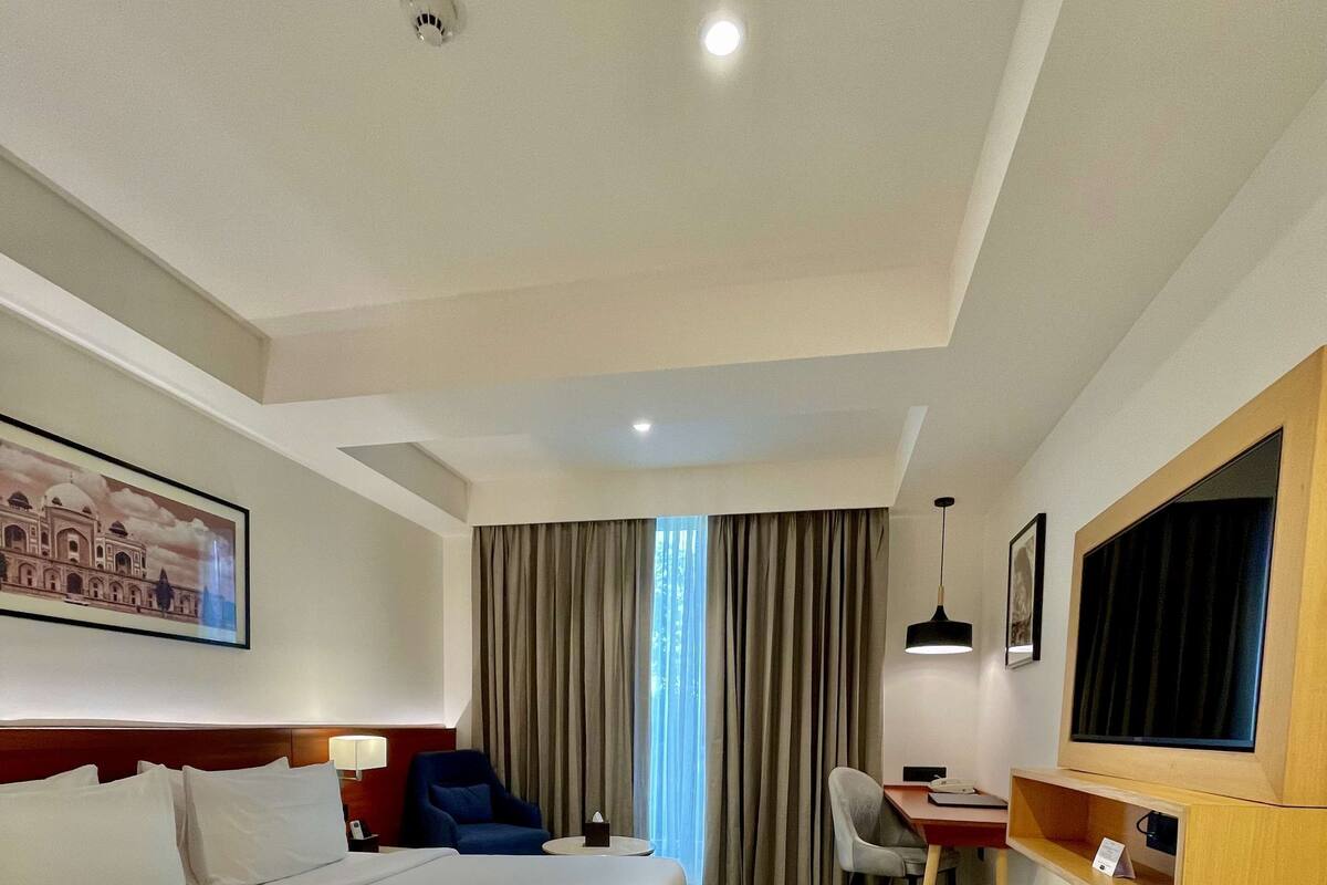 A hotel room with a large bed, a desk, a chair, a television, and a painting on the wall.