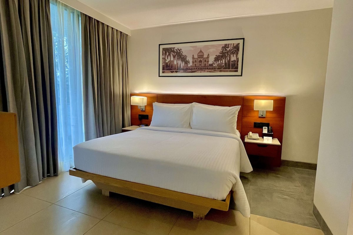 A hotel room with a large bed, two bedside tables with lamps, a wall-mounted picture, and a window with curtains.