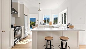 Une cuisine spacieuse dotée d’un grand îlot central, de meubles blancs et offrant une vue sur un paysage montagneux.