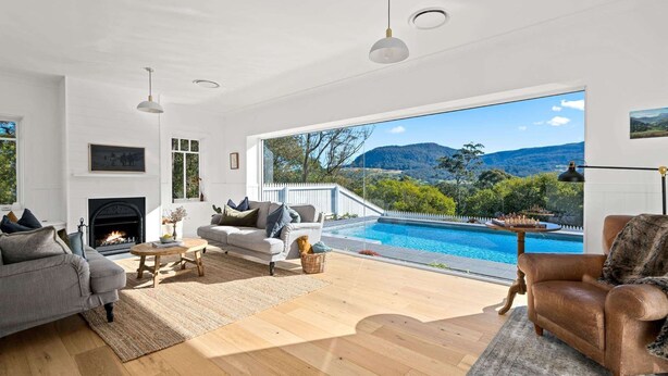 Un salon spacieux avec une cheminée, une grande fenêtre donnant sur une piscine et les montagnes, et un coin salon confortable.