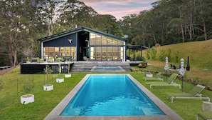 Ett modernt hus med en stor glasfasad, en swimmingpool och en uteplats.