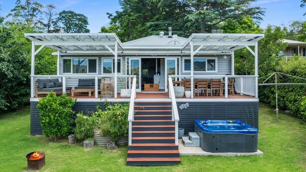 Ein zweistöckiges Haus mit überdachter Veranda, Whirlpool und Feuerstelle im Garten.