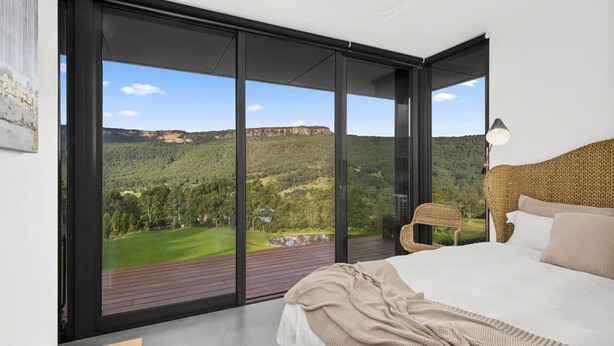 Een slaapkamer met een grote schuifglazen deur naar een balkon, een bed, een stoel en een lamp.