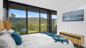 Een slaapkamer met een groot bed, uitzicht op een bergachtig landschap en een schilderij aan de muur.