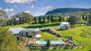 Una casa moderna con piscina, rodeada de exuberante vegetación y colinas.