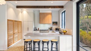 Una cocina moderna con armarios blancos, una isla central con taburetes, una estufa y un ventanal con persianas.