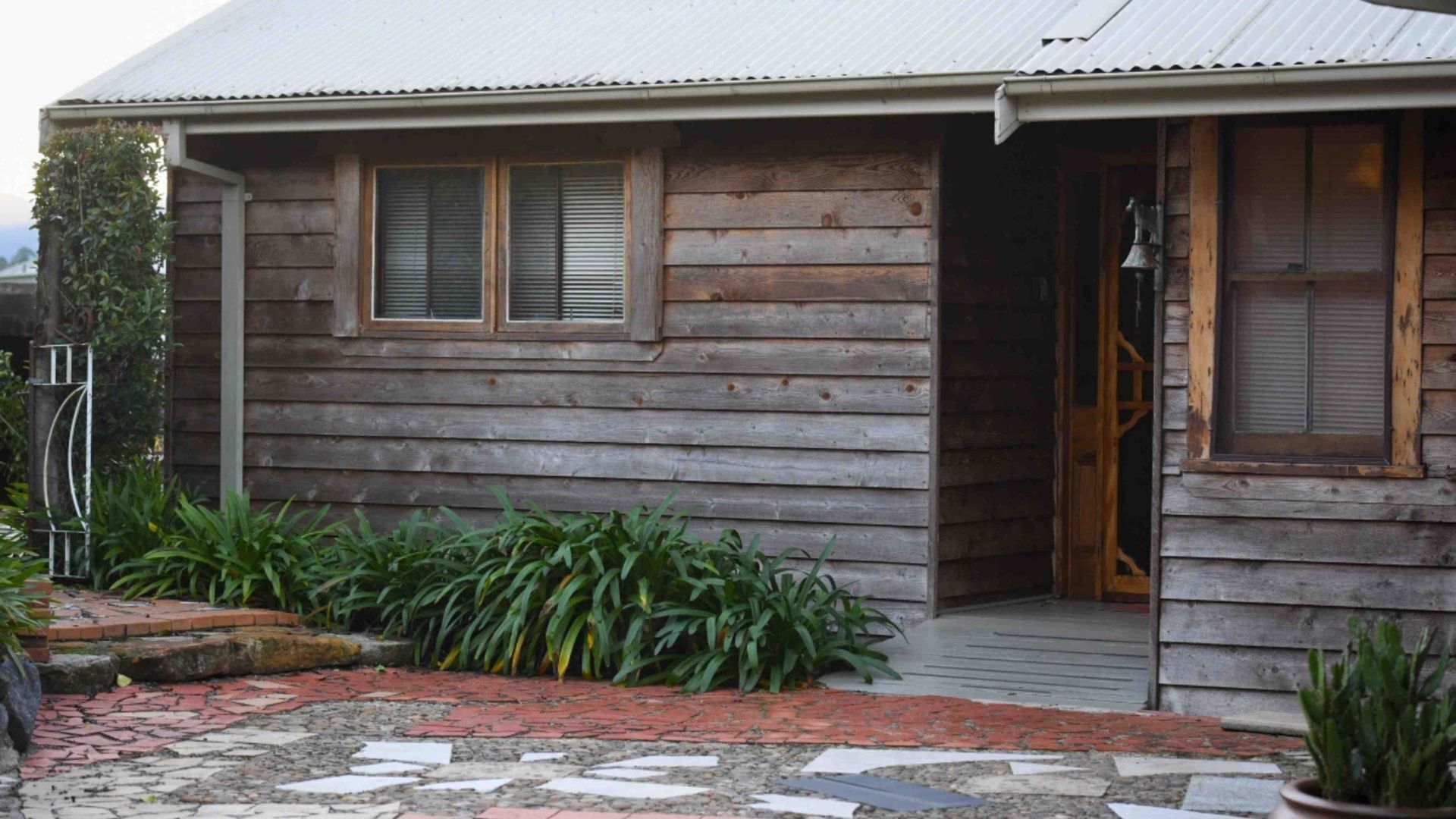 A wooden house with a porch, a small garden, and a brick pathway leading to the entrance.
