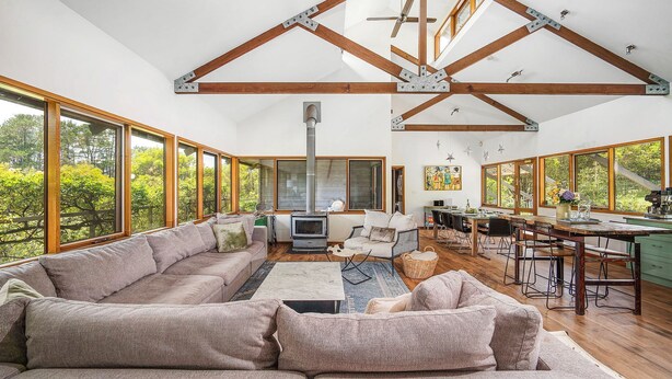 A spacious living area with a high ceiling, large windows, a fireplace, and a dining area. - Kookaburra Hill, Kangaroo Valley (Kangaroo Valley)