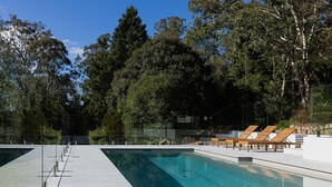 Une piscine avec des chaises longues et une vue sur les arbres.