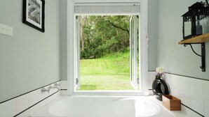 A bathroom with a large bathtub, a toilet, and a sink. There is a window with a view of a grassy area and trees. - Lavender Hill, Kangaroo Valley (Kangaroo Valley)