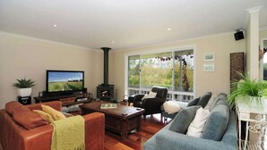 A living room with a television, fireplace, and large windows offering a view of the outdoors. - Lavender Hill, Kangaroo Valley (Kangaroo Valley)