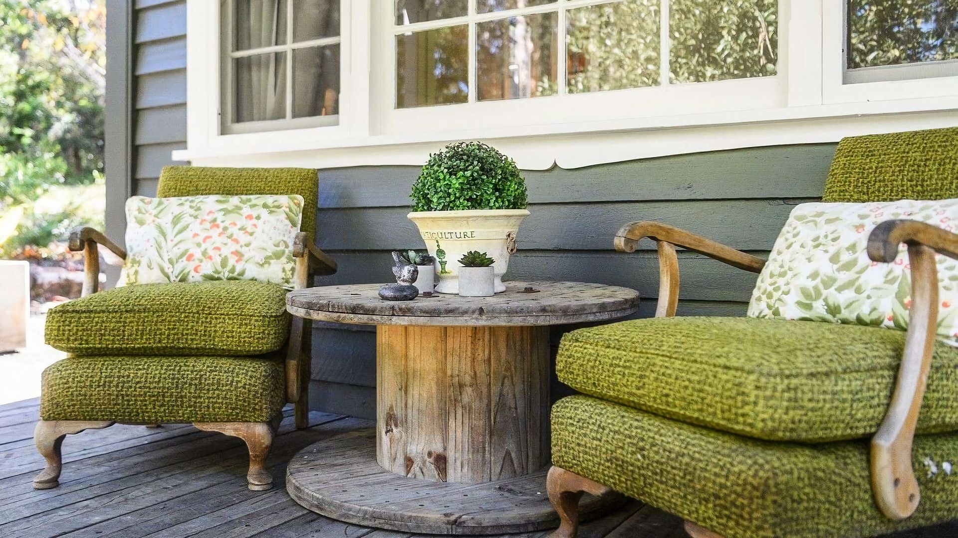 A porch with two green upholstered chairs and a small round wooden table.