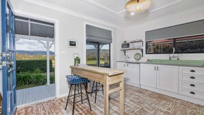 A kitchen with a wooden table, bar stools, a view through the windows, and a white tiled backsplash.