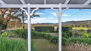 A covered outdoor area with a pergola structure, surrounded by well-maintained hedges and grass.