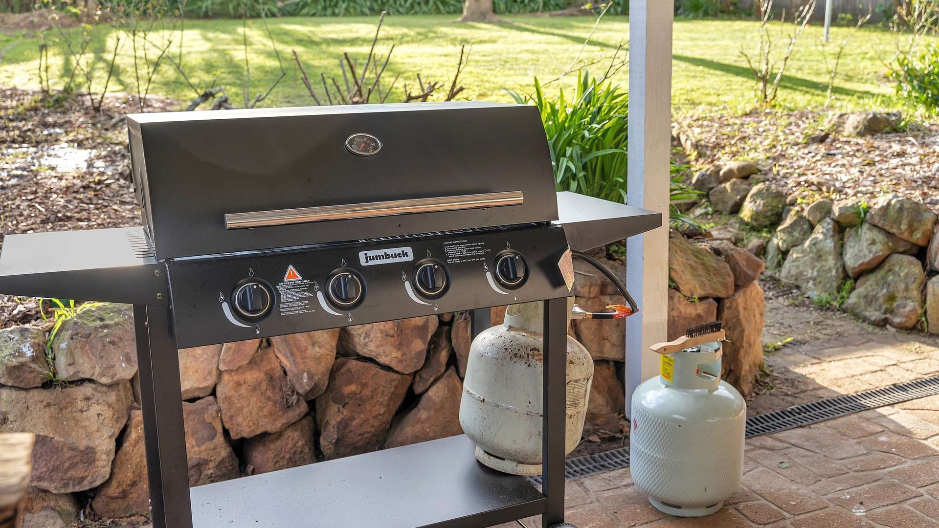 An outdoor grill with four burners, a gas tank, and a metal table.