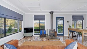 A spacious living room with a large window, a fireplace, a television, and a dining area. - Maddys KV, Kangaroo Valley (Barrengarry, Kangaroo Valley)