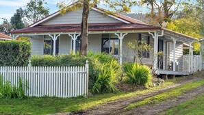 A two-story house with a porch, surrounded by a white picket fence and various plants.