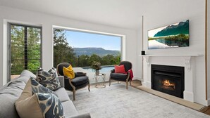Un salon doté d’une cheminée, d’un grand téléviseur et offrant une vue sur une montagne et un lac.