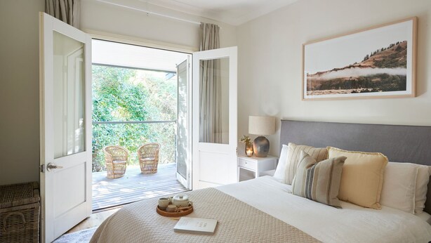 Een hotelkamer met een groot bed, een balkon met rieten stoelen, een schilderij aan de muur en een nachtkastje met een lamp.