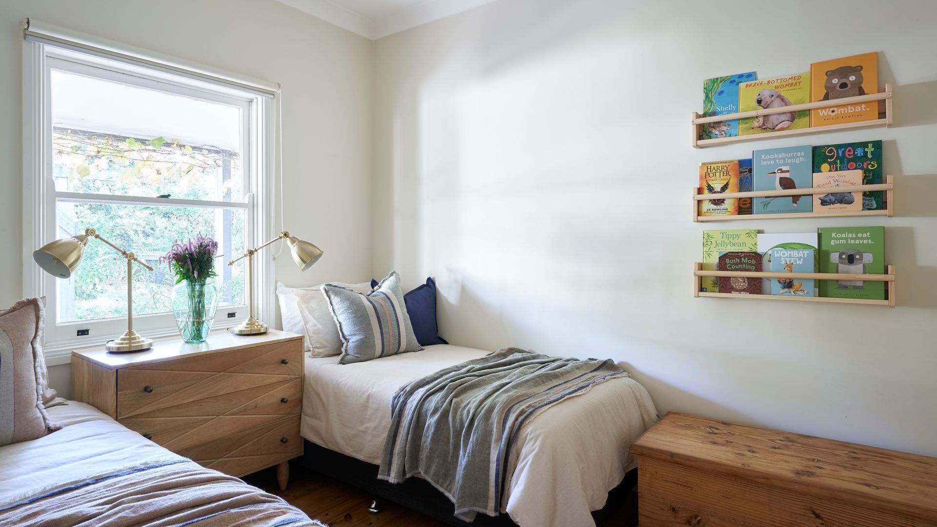 A bedroom with a bed, bedside tables, a window, and a bookshelf with children's books.