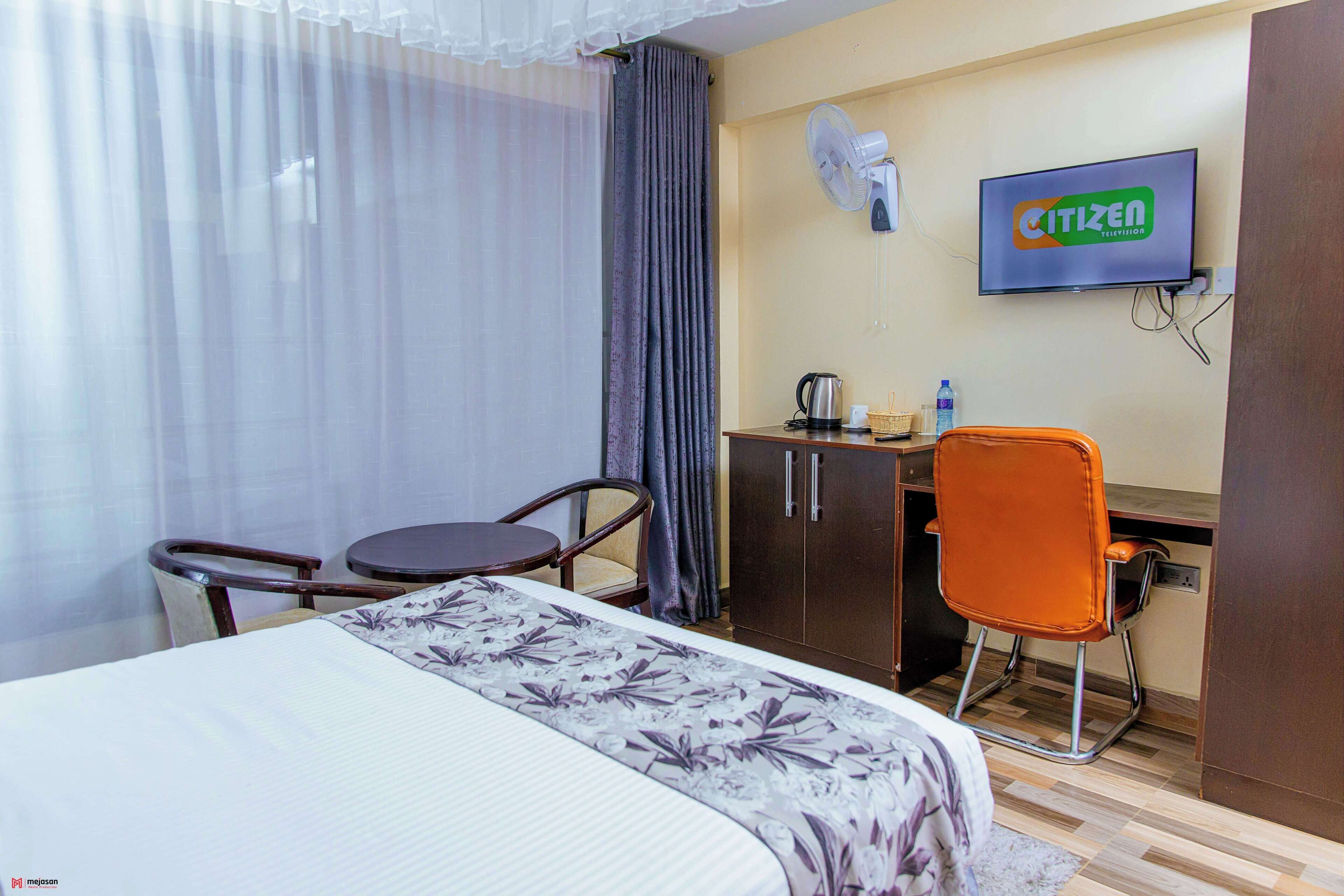 A hotel room with a bed, a desk, a chair, a television, and a fan.