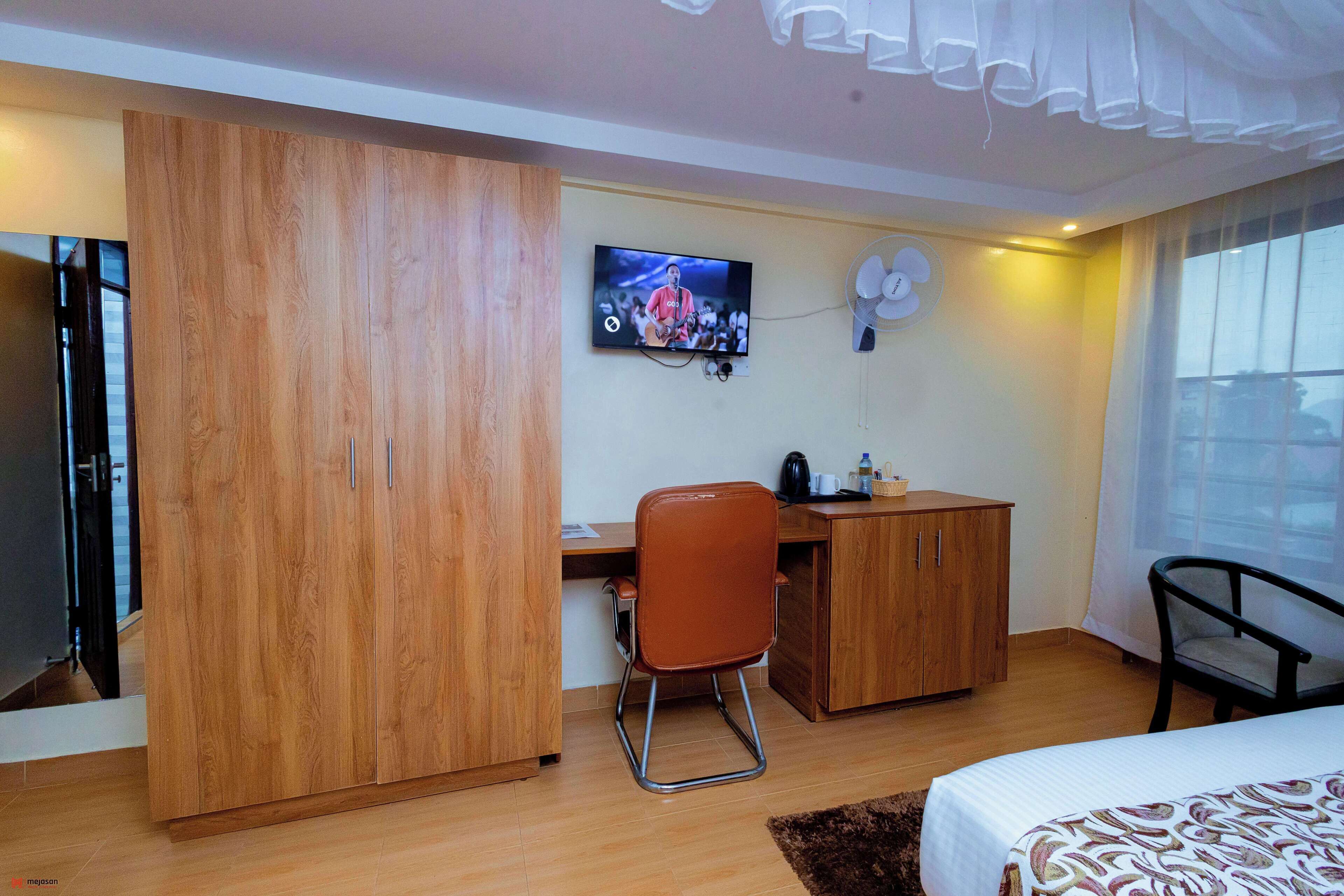 Habitación de hotel con cama, escritorio, silla, armario, televisor y ventana.