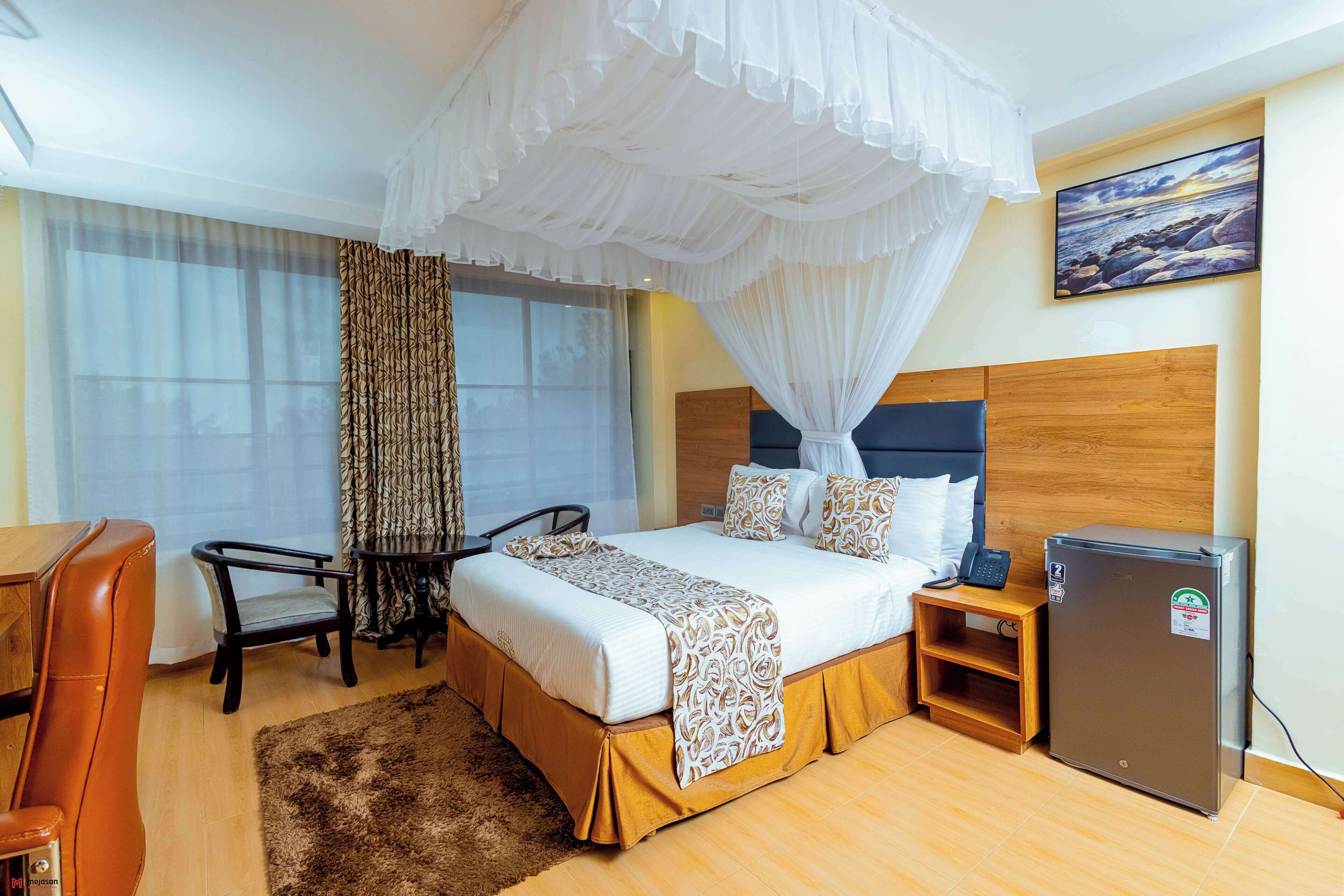 Ein Hotelzimmer mit Bett, Schreibtisch, Stuhl, Kühlschrank und einem großen Fenster mit Vorhängen.
