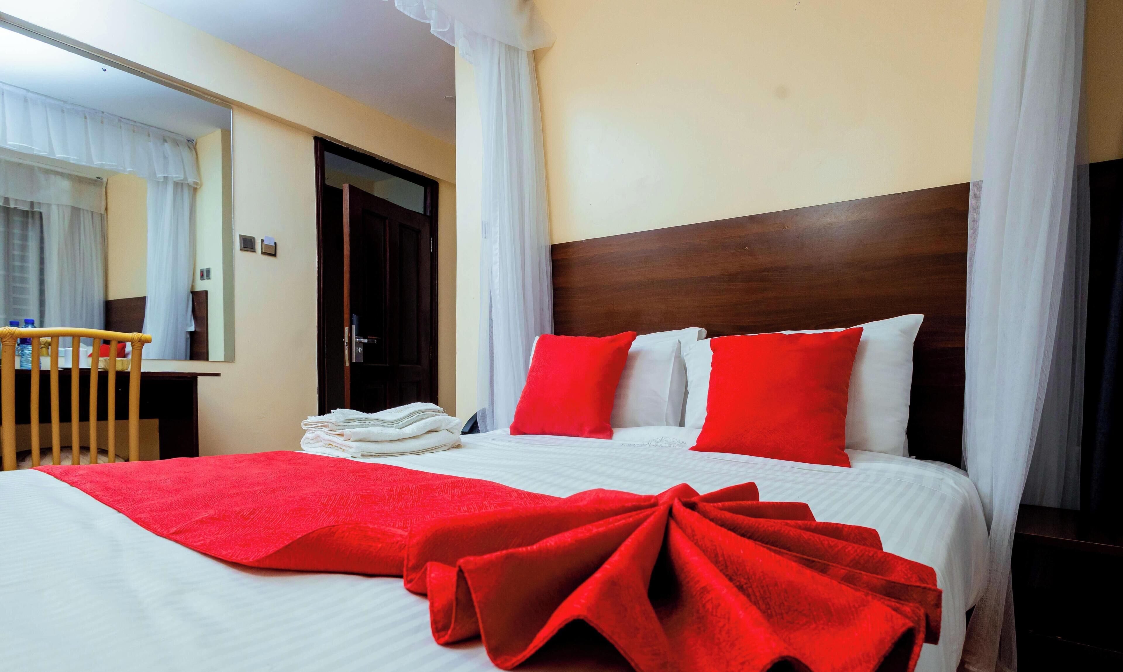 A hotel room with a bed, a wooden headboard, a red and white bedspread, and a window with curtains.