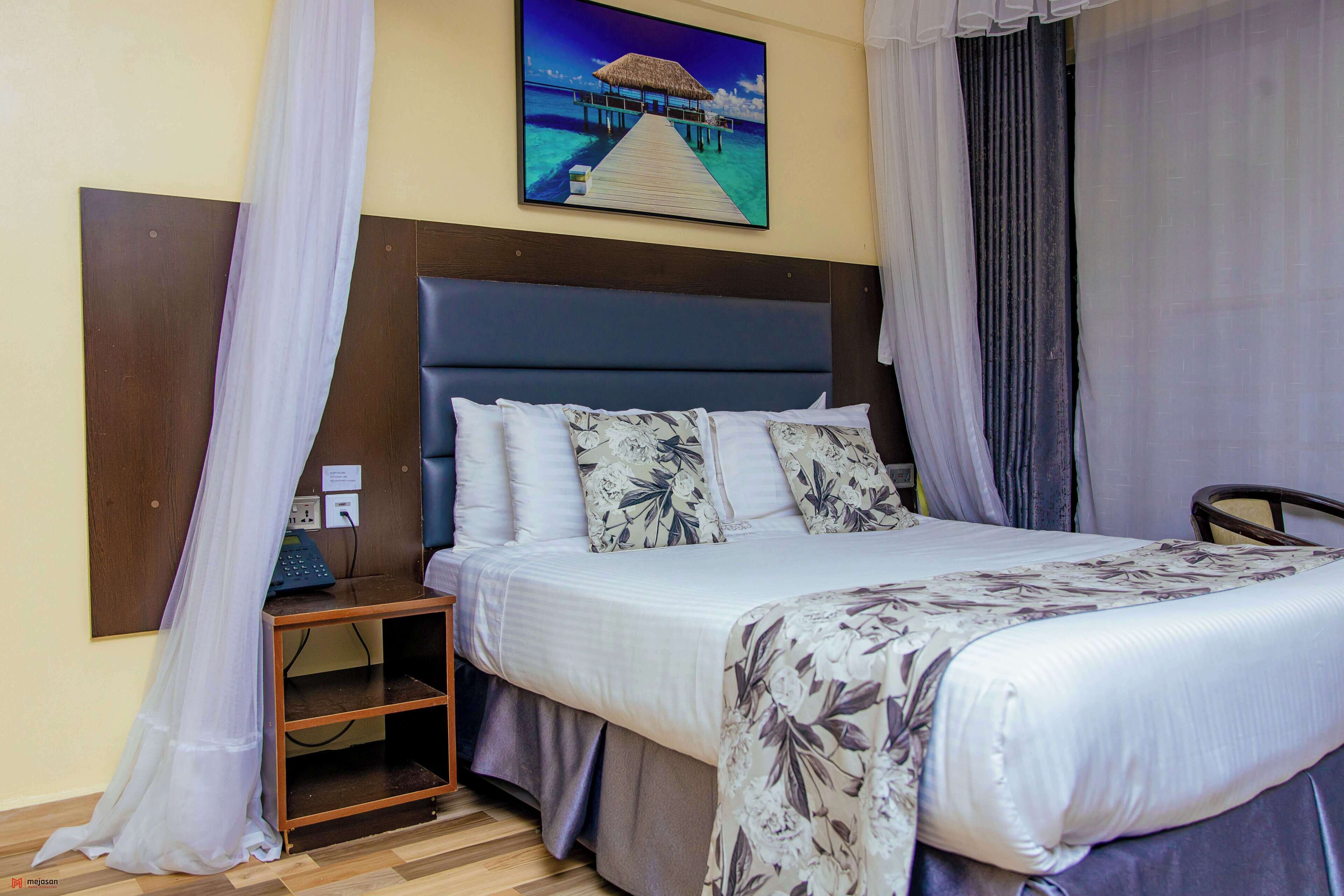 Habitación de hotel con cama, mesita de noche, teléfono y un cuadro de una playa.