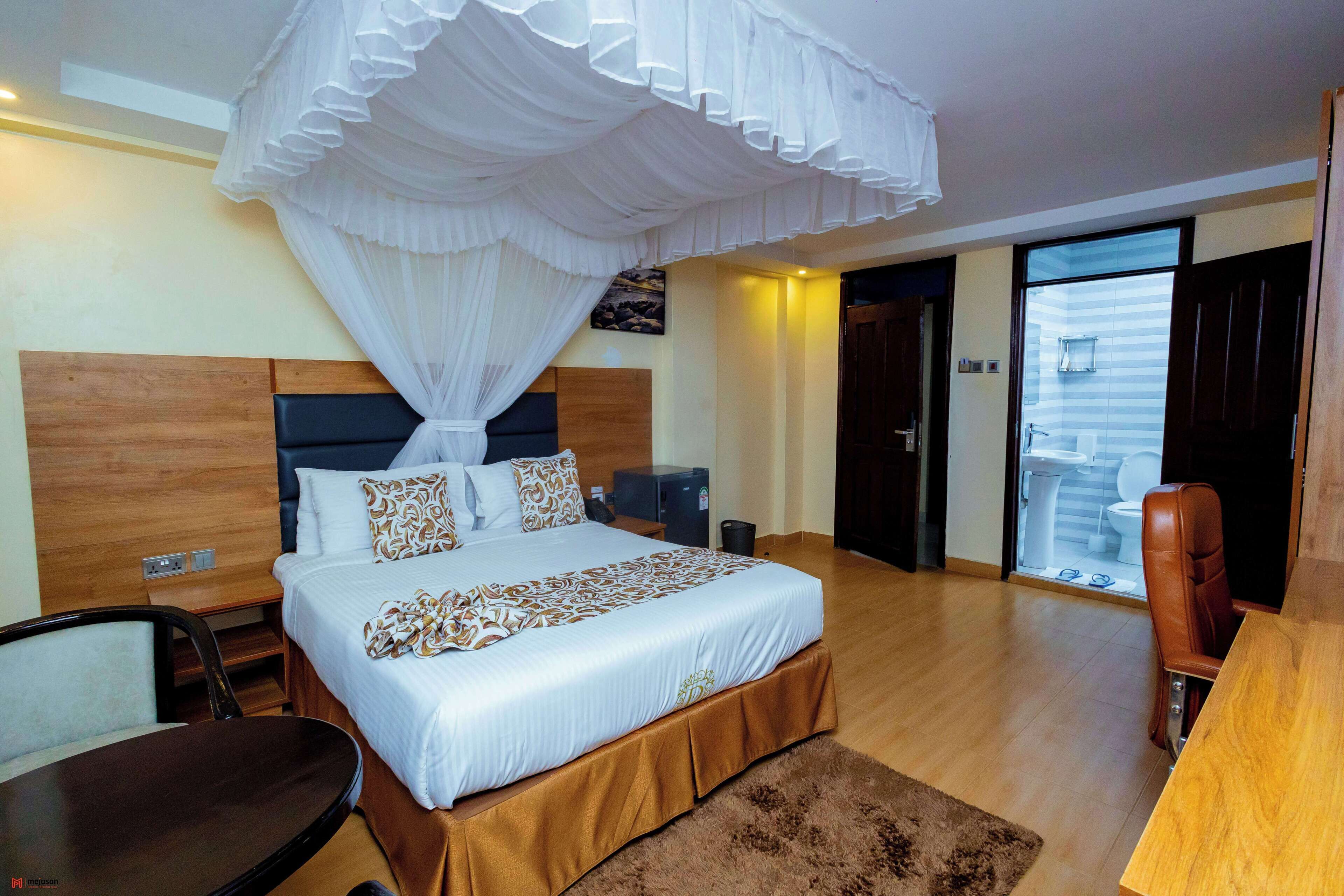 A hotel room with a bed, bedside table, chair, and a view of the outside through a door.