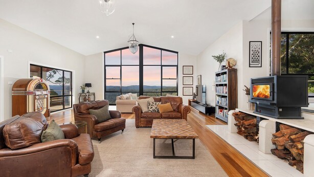A spacious living room with leather sofas, a coffee table, a fireplace, and a large window offering a scenic view. - Valley View Estate, Kangaroo Valley (Beaumont, Kangaroo Valley)