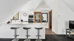 A modern kitchen with a central island, bar stools, a large window, and a TV. - Valley View Studio, Kangaroo Valley (Beaumont, Kangaroo Valley)