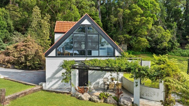 A modern house with a triangular roof, large windows, and a patio with outdoor furniture. - Valley View Studio, Kangaroo Valley (Beaumont, Kangaroo Valley)