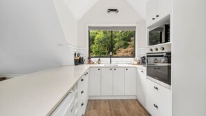 A modern kitchen with white cabinetry, a large window, and a built-in oven. - Valley View Studio, Kangaroo Valley (Beaumont, Kangaroo Valley)